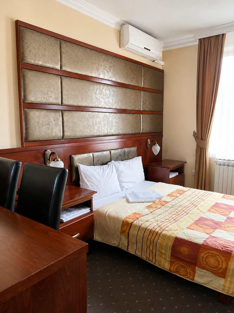 Gostinjska soba u Hotelu Kamel u Banja Luci s bračnim krevetom, drvenim uzglavljem i toplim osvjetljenjem